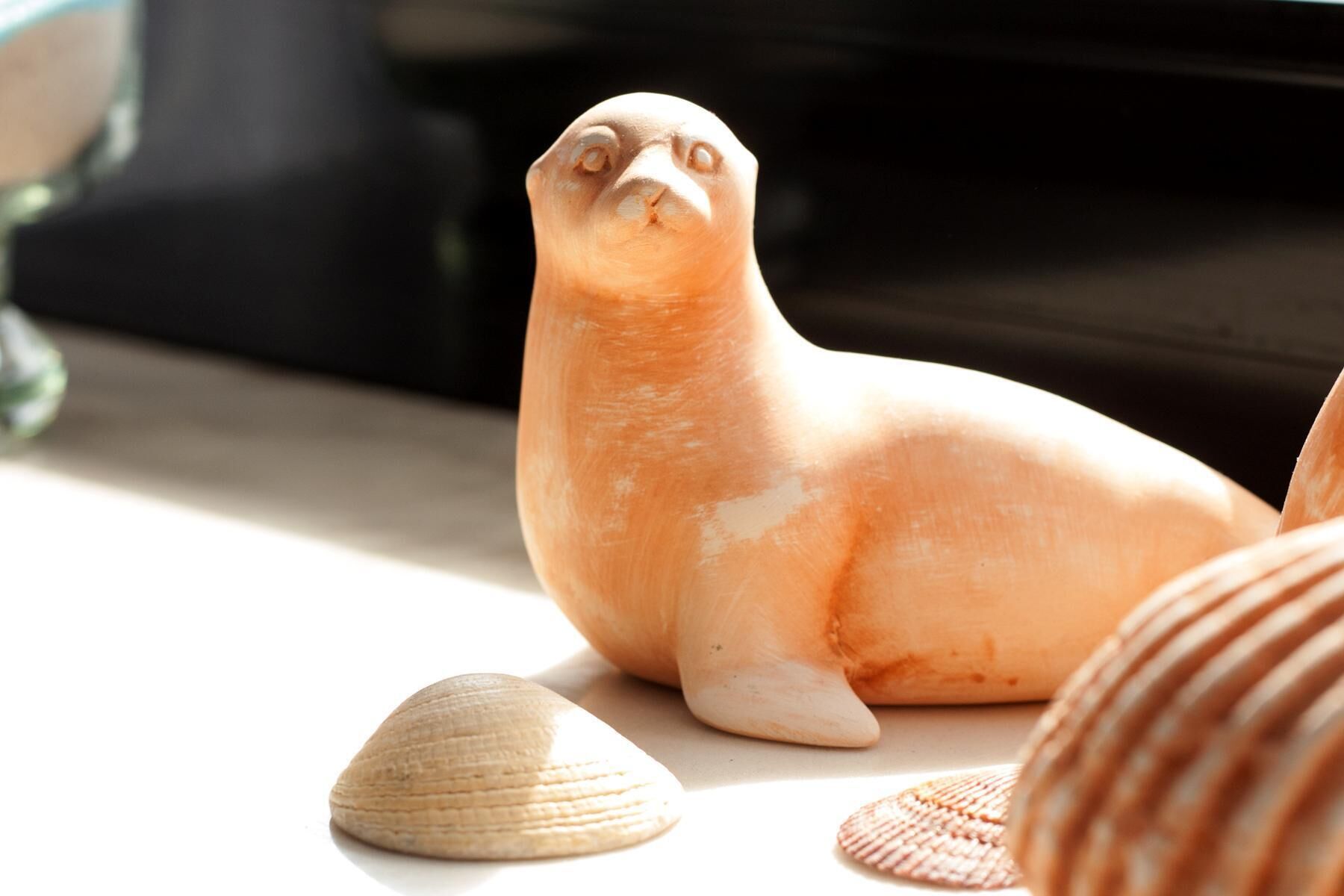 Una figurita de foca sobre una mesa con conchas marinas a su alrededor.