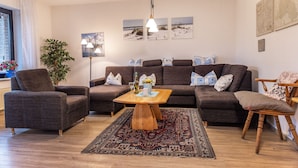 Un salon avec un ensemble de canapés marron, une table basse en bois et un tapis à motifs.