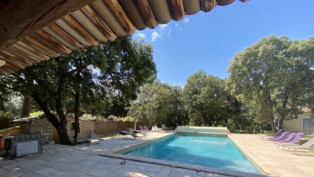 Una piscina con sillas de descanso, zona de barbacoa y porche cubierto.