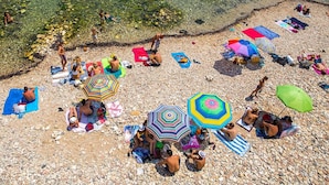 A pebble beach with clear water, people sunbathing, and colorful umbrellas. - Fully furnished apartment, with all comforts. ALL INCLUSIVE (Siracusa)