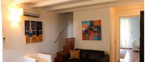 A living room with a white armchair, a dark sofa, and two colorful abstract paintings on the walls.
