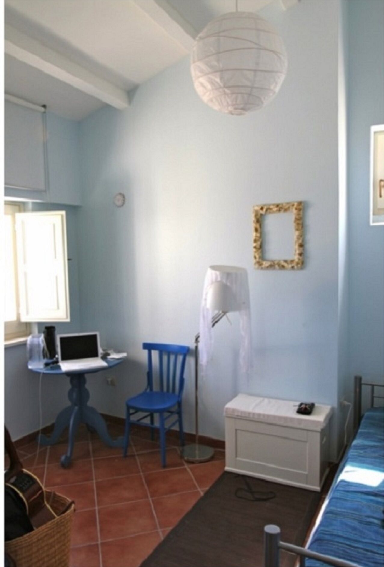 Une pièce avec une chaise bleue, un petit bureau avec un ordinateur portable, une armoire blanche et un luminaire suspendu.