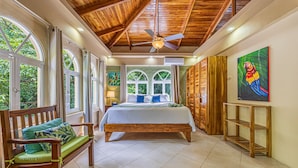 A spacious bedroom with a wooden ceiling, large windows, a bed with a white bedspread, and a colorful painting on the wall. - Casa Bamboo | 4-Bedroom Colonial Jungle Villa | Private Pool | Manuel Antonio (Manuel Antonio)