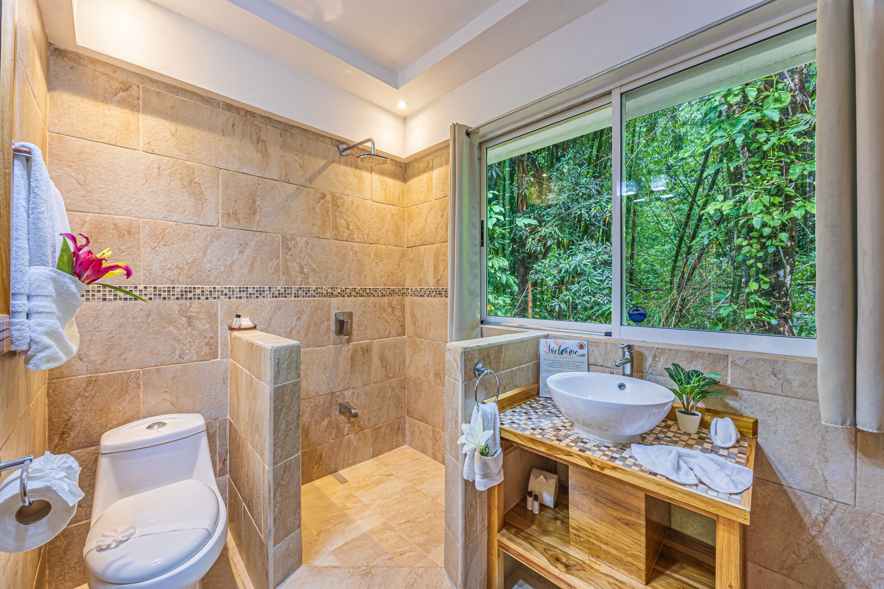 A bathroom with a large window, a shower, a toilet, and a sink.