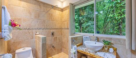 A bathroom with a large window, a shower, a toilet, and a sink.