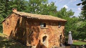 Un edificio rústico de piedra con techo de tejas, un pequeño porche y mobiliario exterior.