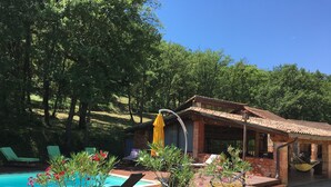 Un área junto a la piscina con sillones reclinables, un edificio pequeño con tejado de baldosas y plantas en macetas.