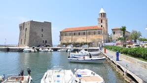 Un port amb embarcacions amarrades, un edifici històric amb una torre campanar i una paret de pedra.