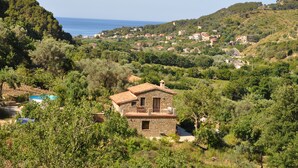 Una casa de pedra amb un balcó, envoltada de vegetació exuberant i vistes al mar.