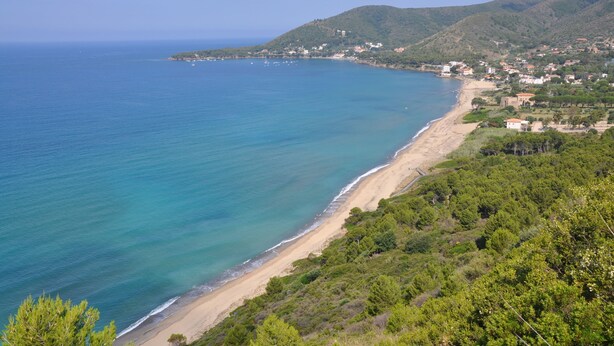 Paisatge costaner amb una platja, cel serè i un fons d'hivernació amb turons.