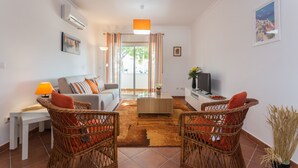 Ein Wohnzimmer mit einer Couch, zwei Korbstühlen, einem Couchtisch und einem Fernseher auf einem Schrank.