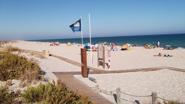 Ein Strand mit einer Flagge, einem Holzsteg und Menschen, die sonnenbaden.