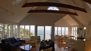 Ampla sala de estar com teto alto, grandes janelas e vista para o mar.