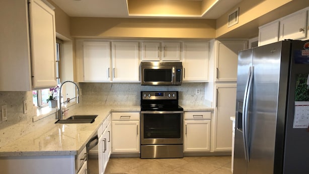 A modern kitchen with white cabinets, stainless steel appliances, a microwave, oven, and refrigerator. - Newly Renovated Vacation Home With Desert Theme in Premier Golf Community (Sun City West)