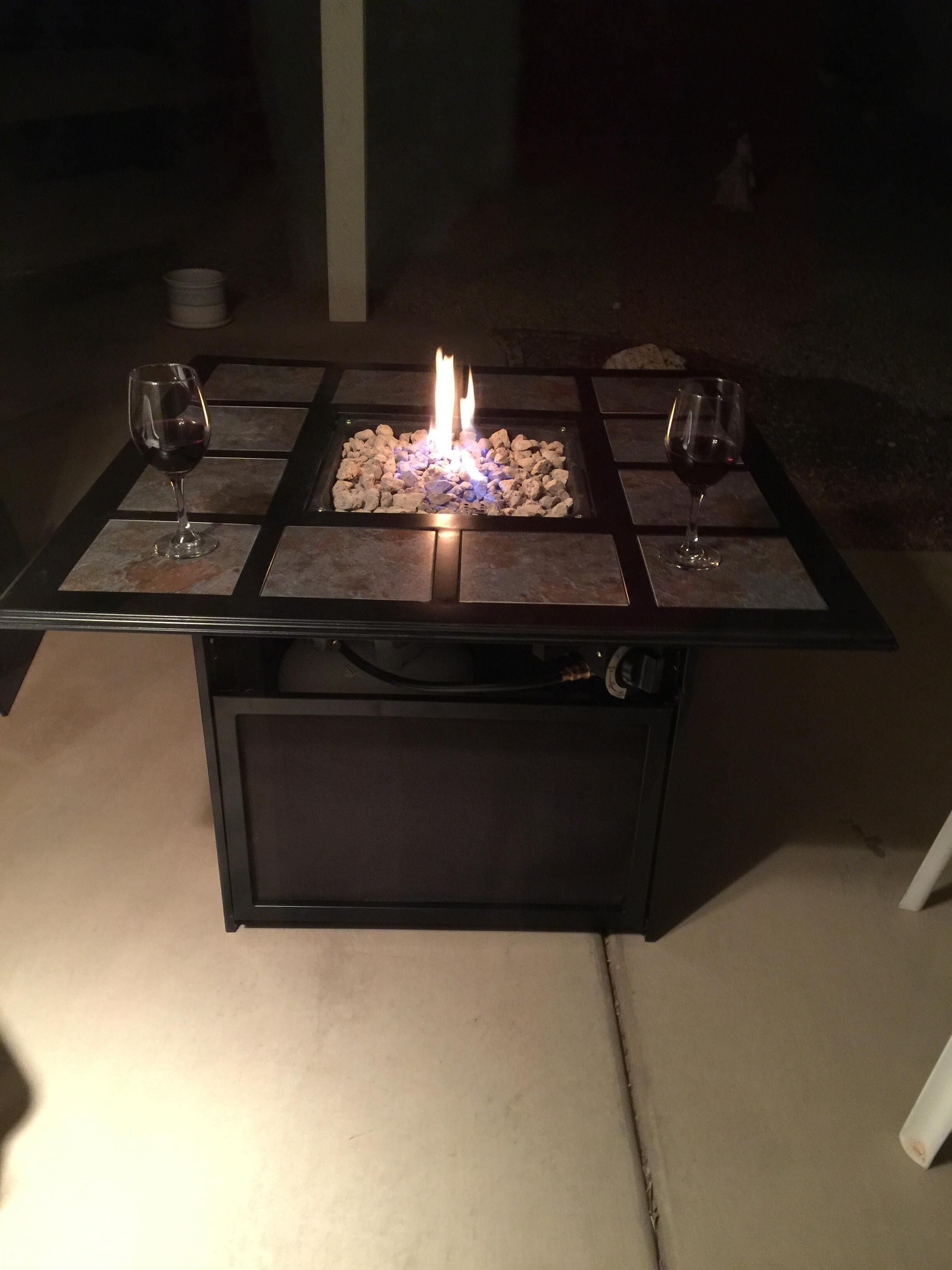 An outdoor fire feature with two glasses of wine on a square table.