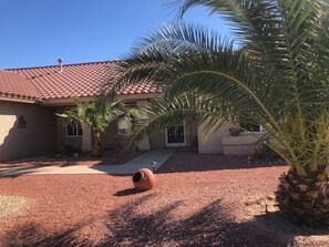 Stroll through the beautifully maintained garden, featuring a palm tree and cactus, to the single-story house with a welcoming front entrance.