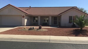 A two-story building with a tiled roof, a front porch, and a landscaped front yard with rocks and a palm tree. - Newly Renovated Vacation Home With Desert Theme in Premier Golf Community (Sun City West)
