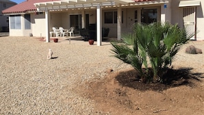 A house with a red-tiled roof, a covered patio with outdoor furniture, and a small palm plant in the front. - Newly Renovated Vacation Home With Desert Theme in Premier Golf Community (Sun City West)