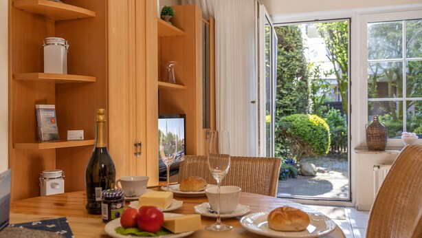 Une table à manger dressée avec des assiettes, une bouteille et des verres, donnant sur un jardin par une fenêtre.
