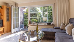 Un salon avec une table basse en verre, un canapé gris et une grande fenêtre avec des rideaux.