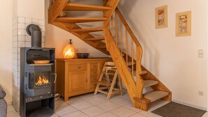 Une pièce chaleureuse avec un poêle à bois, un escalier en bois et un buffet.