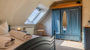 Une chambre avec un puits de lumière, un lit avec des serviettes enroulées, une chaise en bois et une armoire bleue.