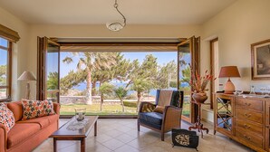 A spacious living area with a sofa, a coffee table, and a chair, a wooden cabinet, and a view of the outdoors. - Four-Bedroom Private Family Villa with Pool, 400m from the Beach. Villa Russelia (Kamiros skala)
