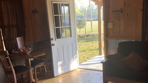 A wooden interior with a door leading outside, a sofa, and a table with chairs. - Cozy Cabin on the Creek with 2 private sandbars (Perkinston)