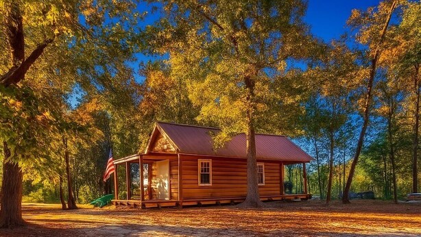 A wooden cabin with a porch, surrounded by trees. - Cozy Cabin on the Creek with 2 private sandbars (Perkinston)