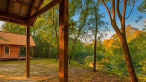 A wooden deck leading to a covered area with a rustic cabin in the background. - Cozy Cabin on the Creek with 2 private sandbars (Perkinston)