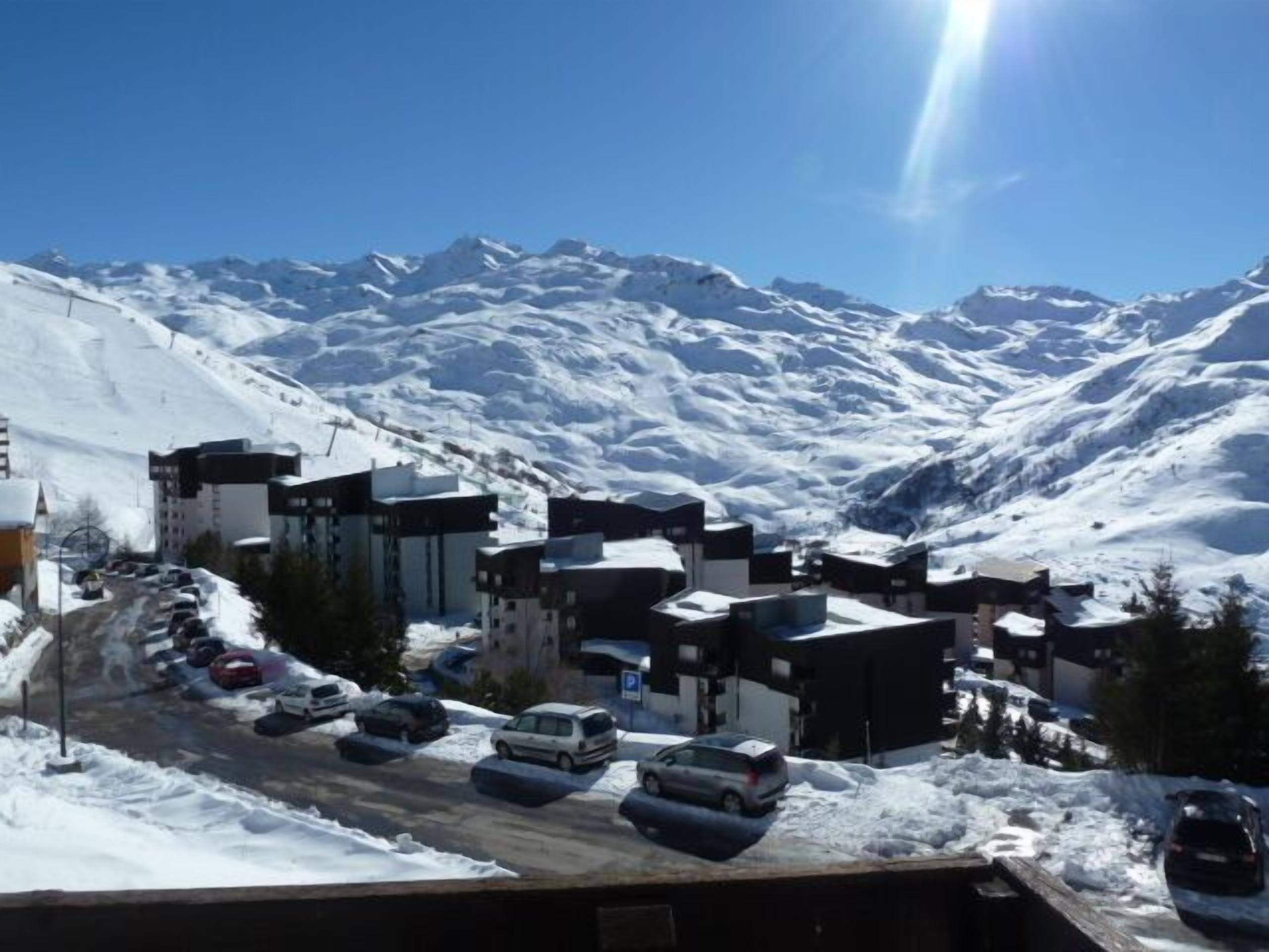 A snow-covered mountain town with modern buildings, a parking lot, and a clear view of the surrounding mountains.