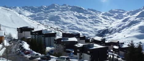 A snow-covered mountain town with modern buildings, a parking lot, and a clear view of the surrounding mountains.