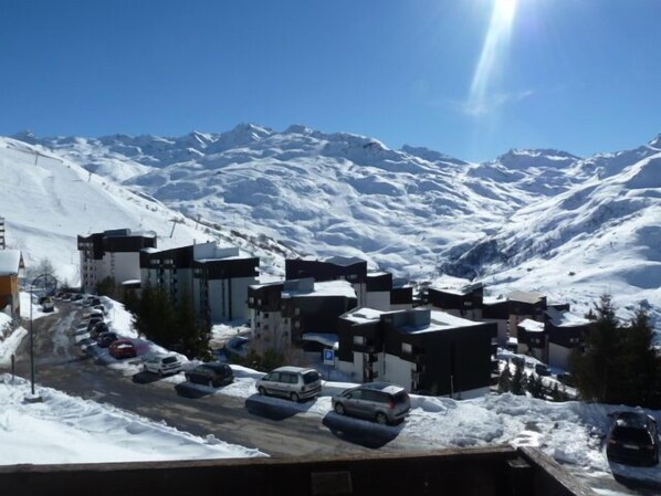 A snow-covered mountain town with modern buildings, a parking lot, and a clear view of the surrounding mountains.