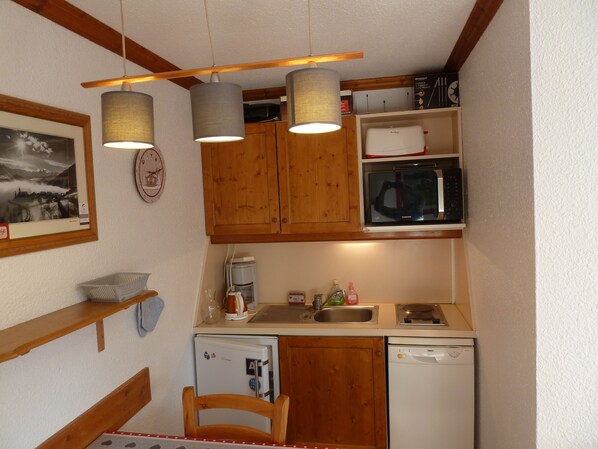 A compact kitchen with wooden cabinets, a microwave, a dishwasher, and hanging pendant lights. - LES MENUIRES APARTMENT, 2 ROOMS, 4/5 PEOPLE (Les Belleville)
