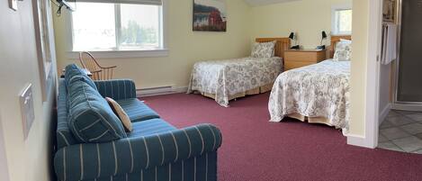 A bedroom with a sloped ceiling, two single beds, a blue striped sofa, a painting on the wall, and a window with blinds.