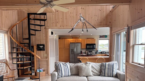 Un interior de madera con una escalera de caracol, un sofá, una mesa de centro y una cocina al fondo.