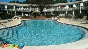 A swimming pool with a curved edge, surrounded by lounge chairs and a building with balconies in the background.