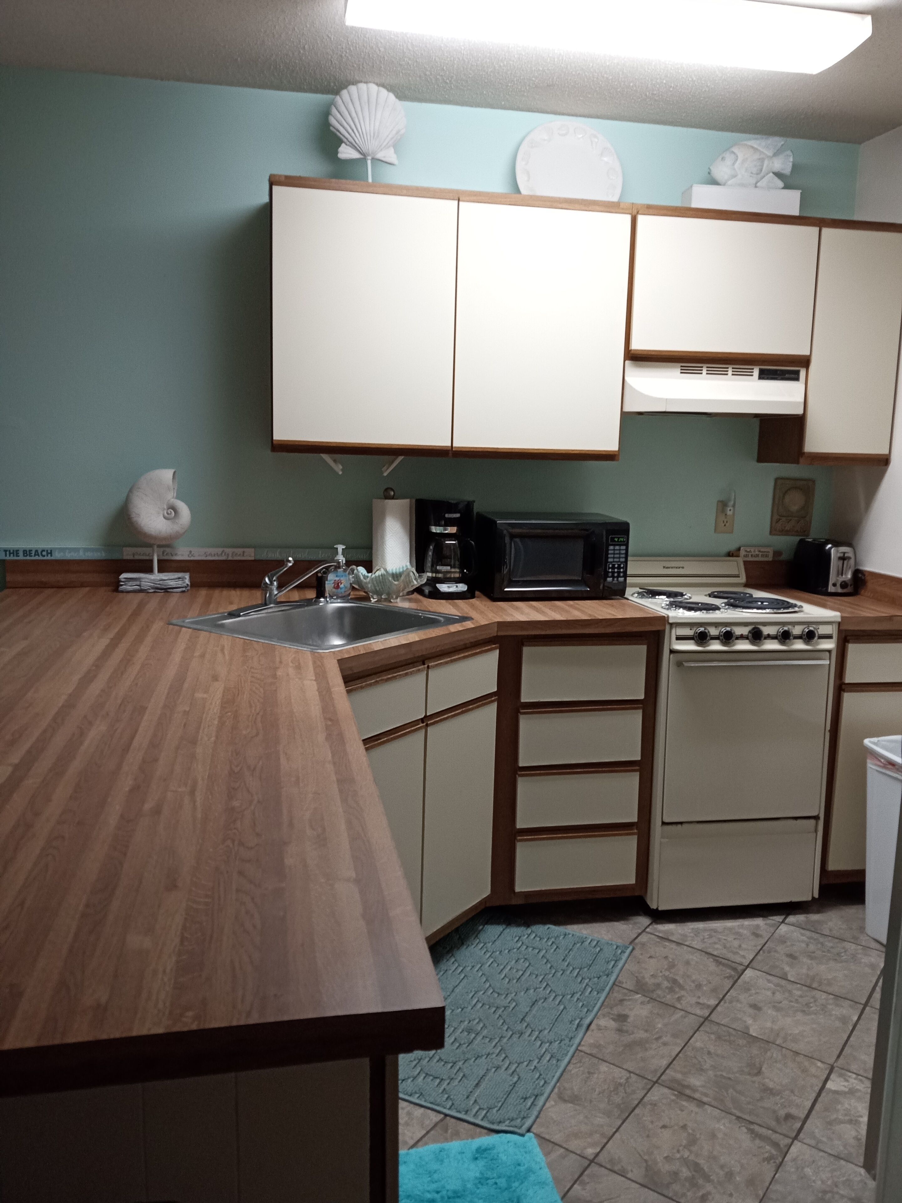 A compact kitchen with wooden countertops, a sink, a microwave, a stove, and cabinets.
