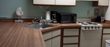 A compact kitchen with wooden countertops, a sink, a microwave, a stove, and cabinets.