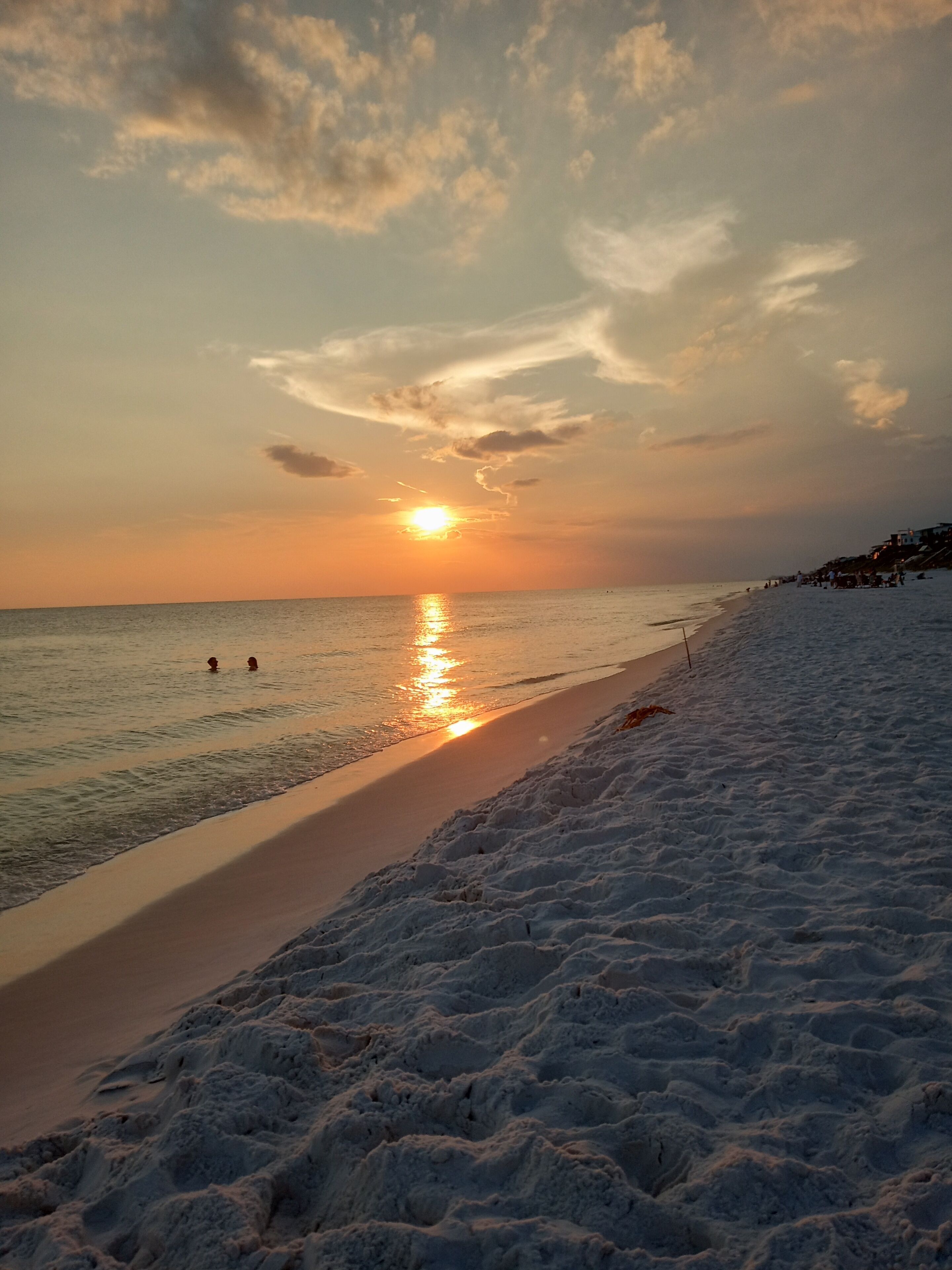 A beach with a sunset, calm sea, and a sandy shore.