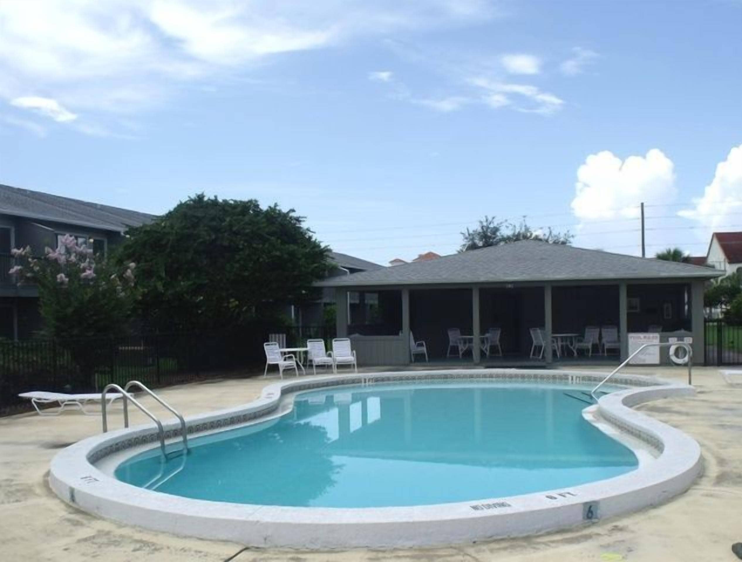 Una piscina amb terrassa coberta, gandules i un edifici al fons.