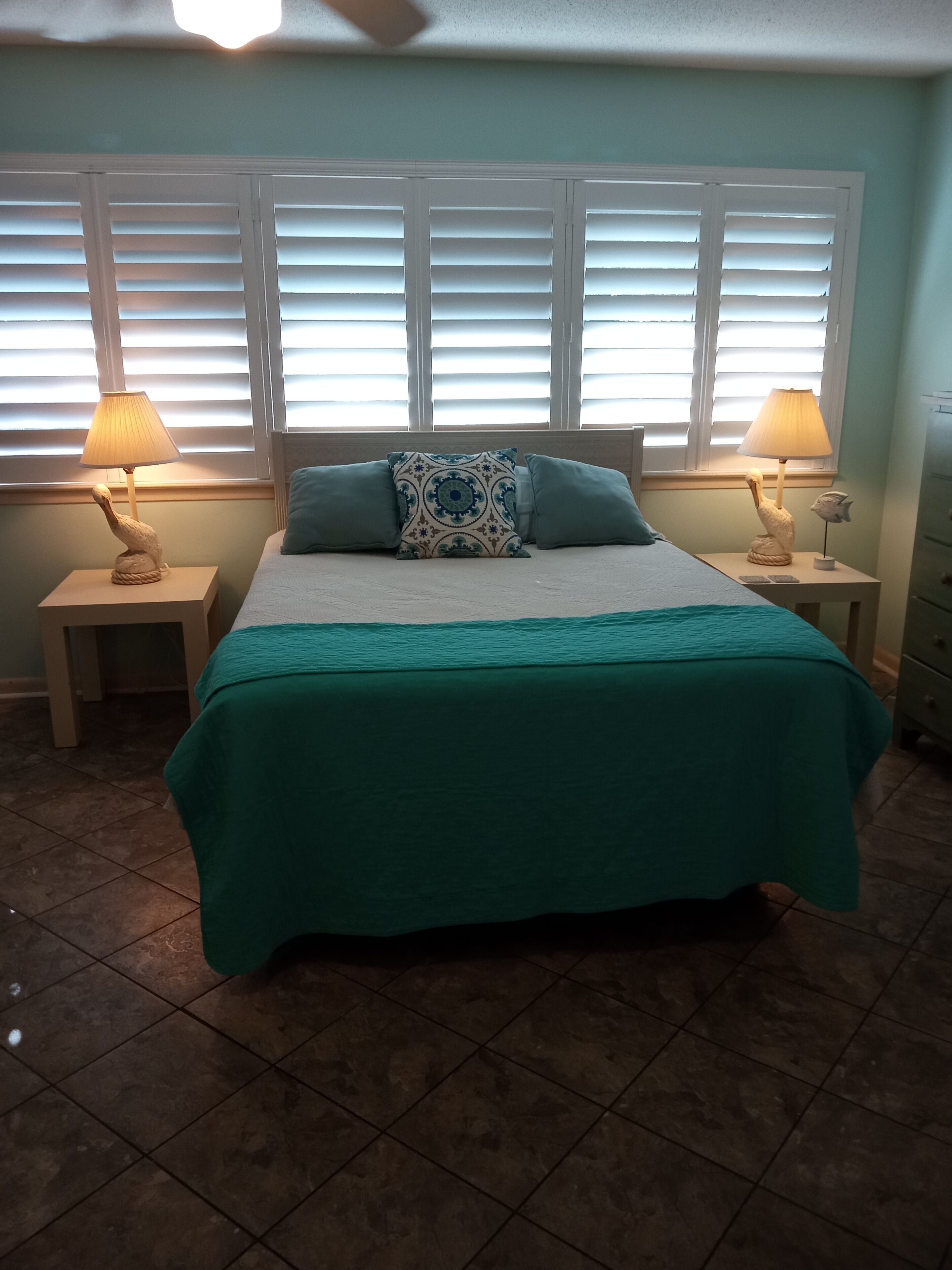 A bedroom with a bed, two nightstands, a lamp, and a window with blinds.