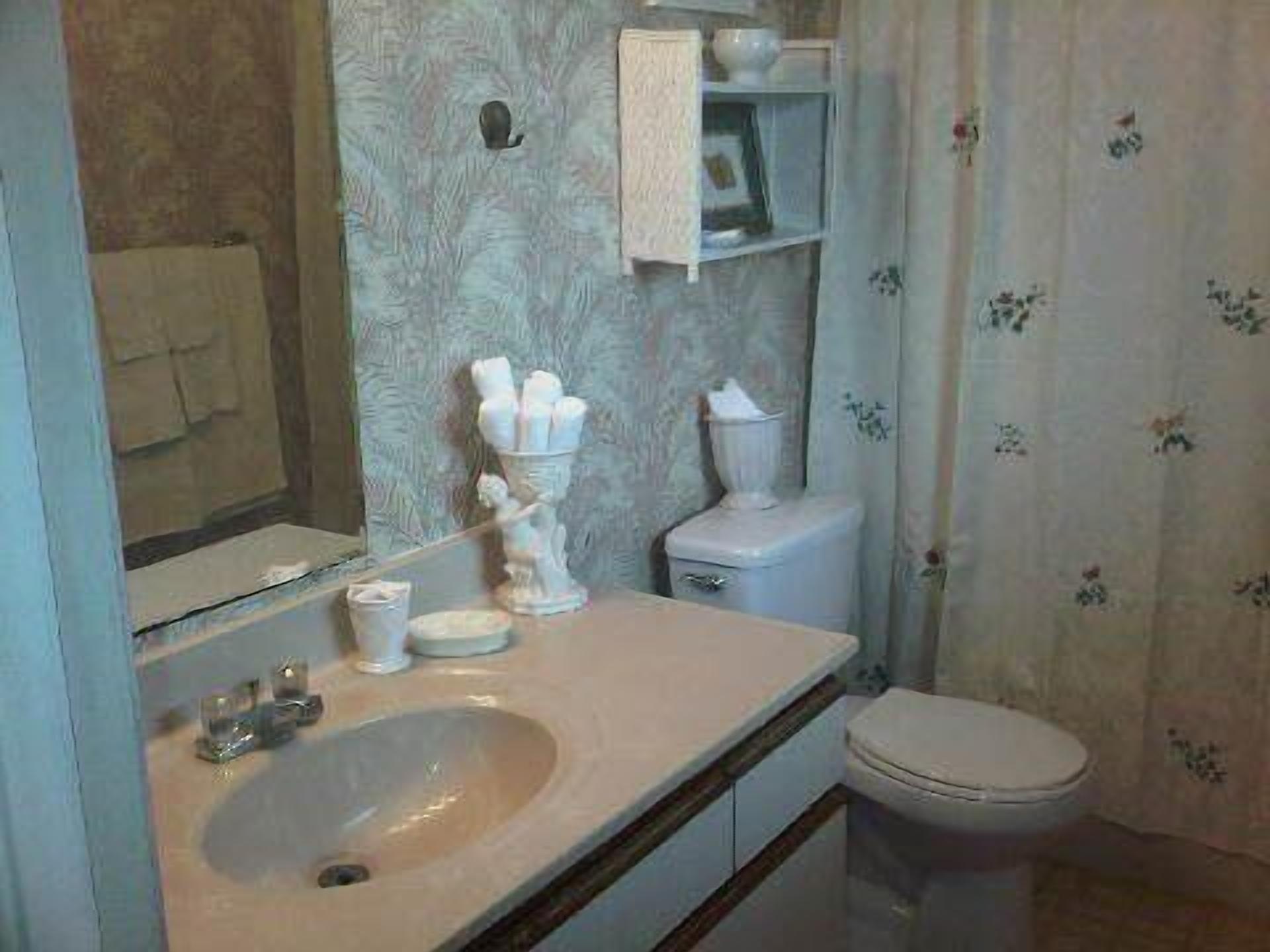 Et badeværelse med vask, spejl, toilet og håndklædestang.