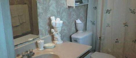 Et badeværelse med vask, spejl, toilet og håndklædestang.