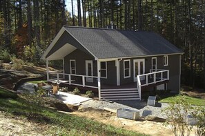 Eine zweistöckige Holzhütte mit Veranda, umgeben von einem Wald.