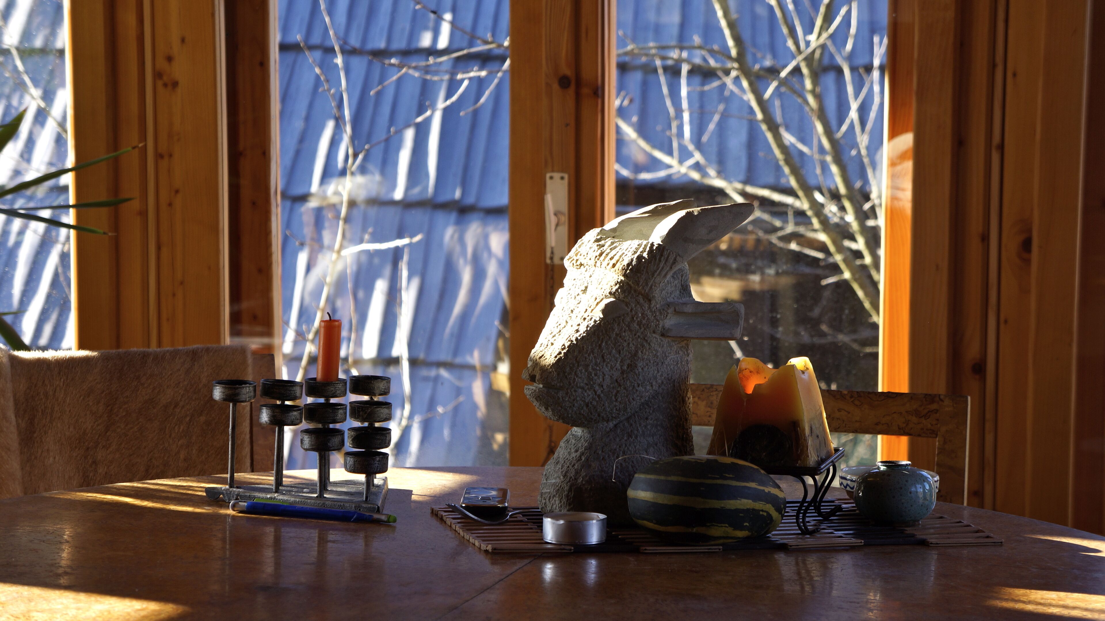 A wooden table with a stone sculpture, a candle holder, and various kitchen items.
