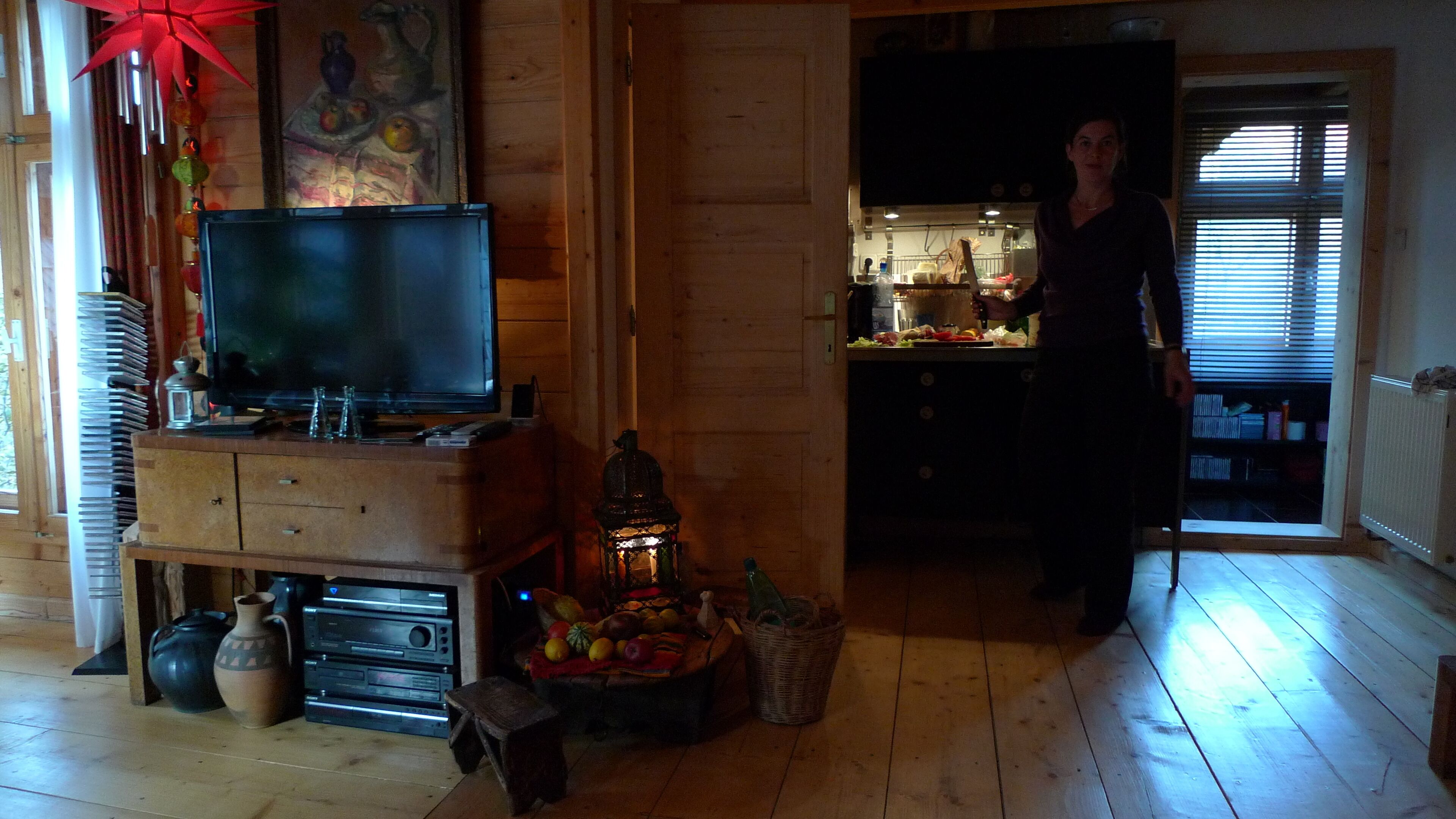 Una sala de estar con televisor, armarios de madera y un comedor con una cocina al fondo.