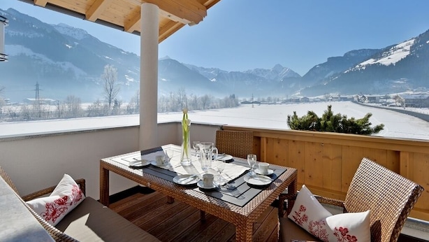 A wooden deck with a table set for dining, overlooking a snowy mountain landscape.