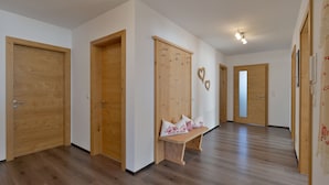 A hallway with wooden doors, a bench with decorative pillows, and a wall-mounted coat rack.