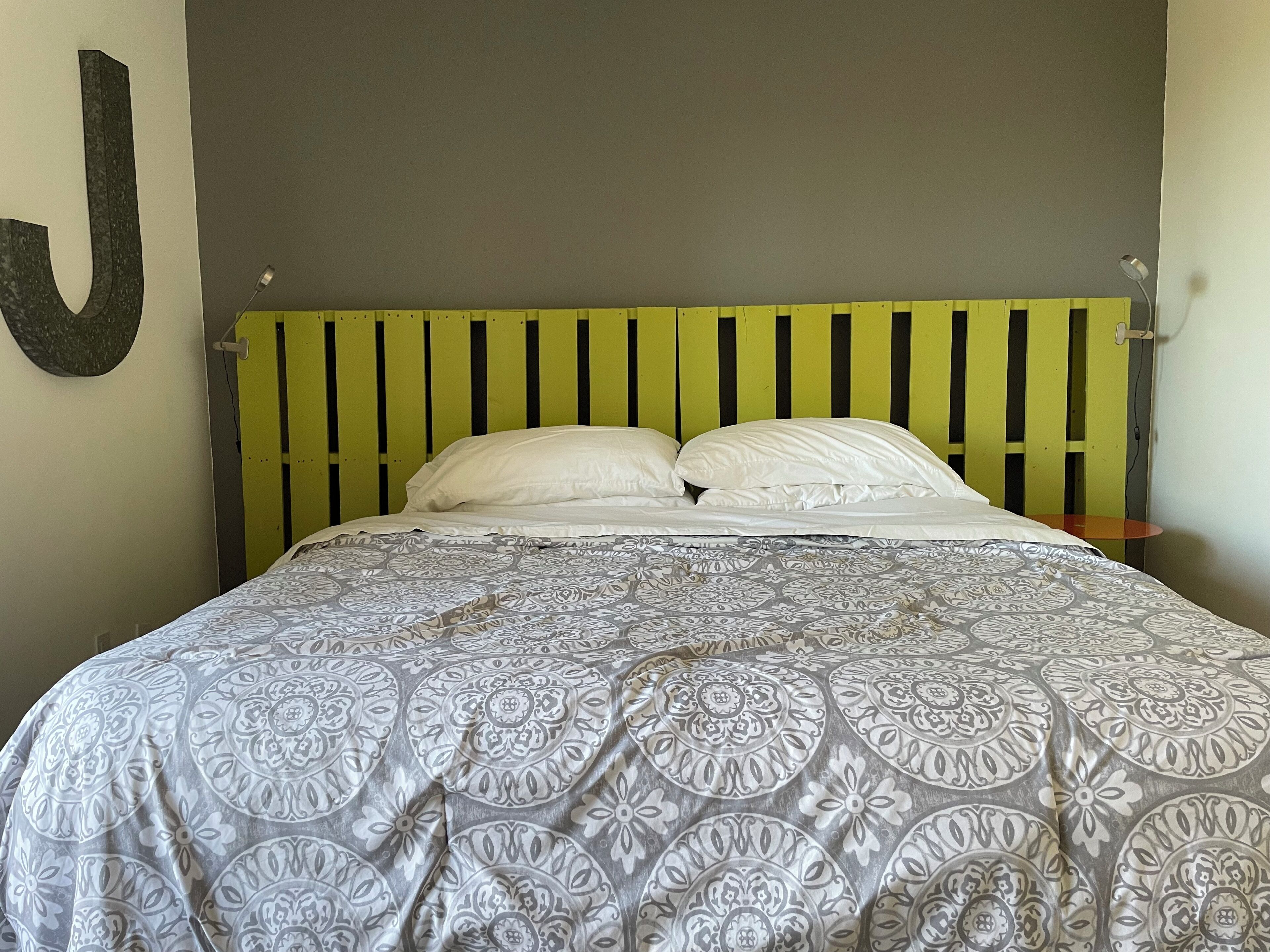A bed with a patterned bedspread, a green and black striped headboard, and a single white pillow.